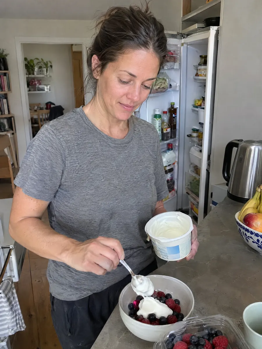 A woman spooning yogurt and berries into a bowl at the kitchen counter